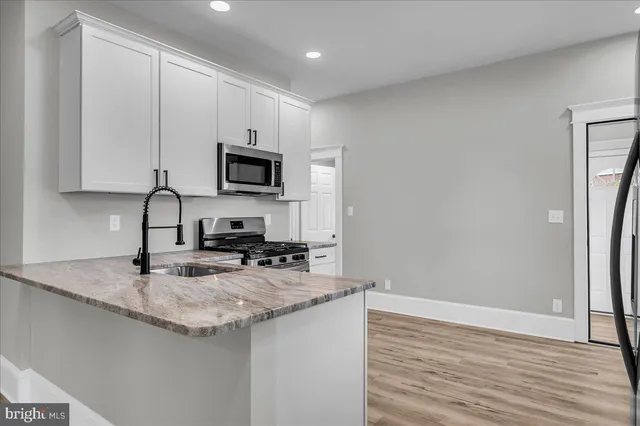 a kitchen with stainless steel appliances granite countertop a stove a sink a refrigerator and white cabinets with wooden floor