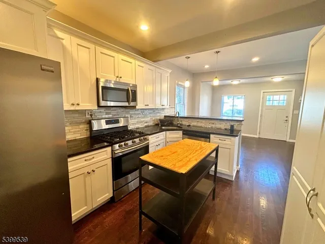 a kitchen with stainless steel appliances granite countertop a stove top oven a sink dishwasher and a refrigerator with wooden floor