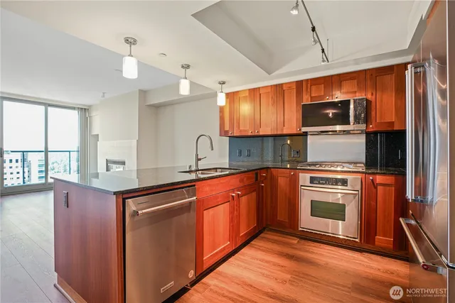 a kitchen with stainless steel appliances granite countertop wooden cabinets a sink a stove a refrigerator and island with wooden floor