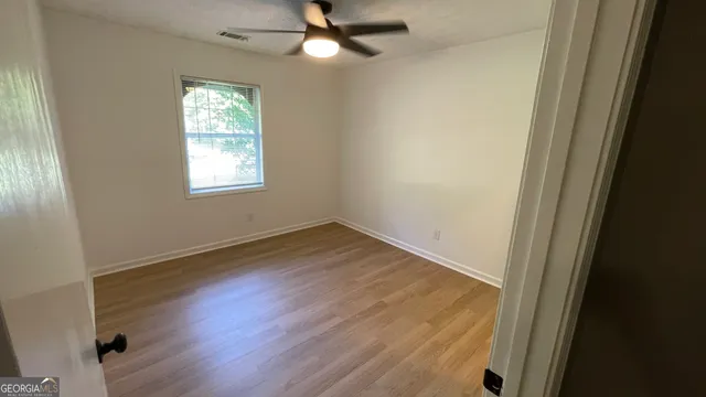 an empty room with wooden floor fan and windows