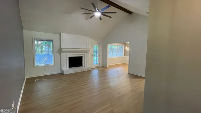 an empty room with wooden floor a ceiling fan a fireplace and windows