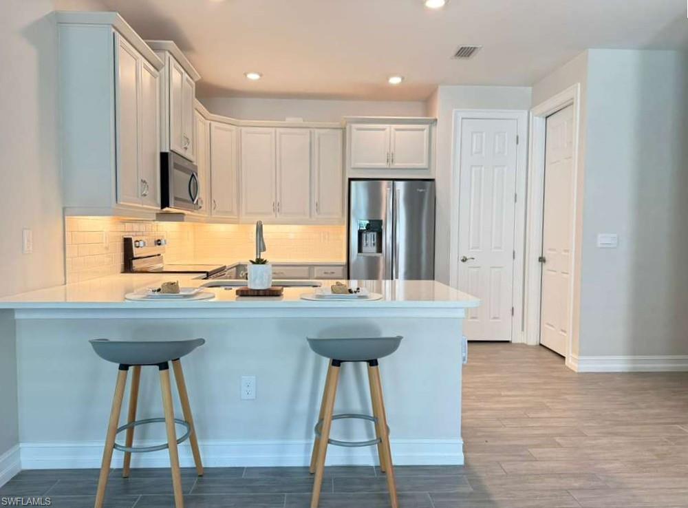 1059 Enbrook Loop Naples, FL 34114 - Photo 3 of 19 Kitchen featuring appliances with stainless steel finishes, a kitchen breakfast bar, tasteful backsplash, a peninsula, and recessed lighting