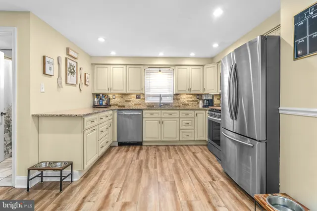 a kitchen with stainless steel appliances granite countertop a refrigerator a sink dishwasher a stove with white cabinets and wooden floor