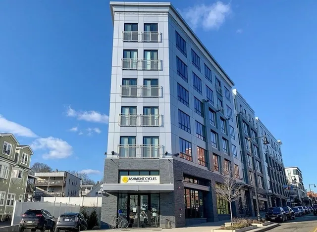 a front view of a building with lot of cars and trees