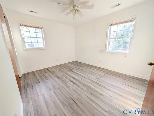 an empty room with wooden floor windows and fan