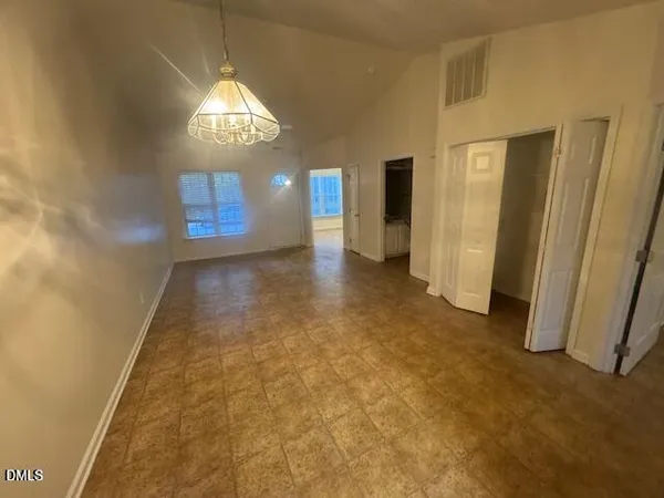 an empty room with chandelier fan and windows