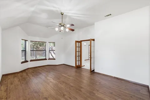 an empty room with wooden floor chandelier fan and windows