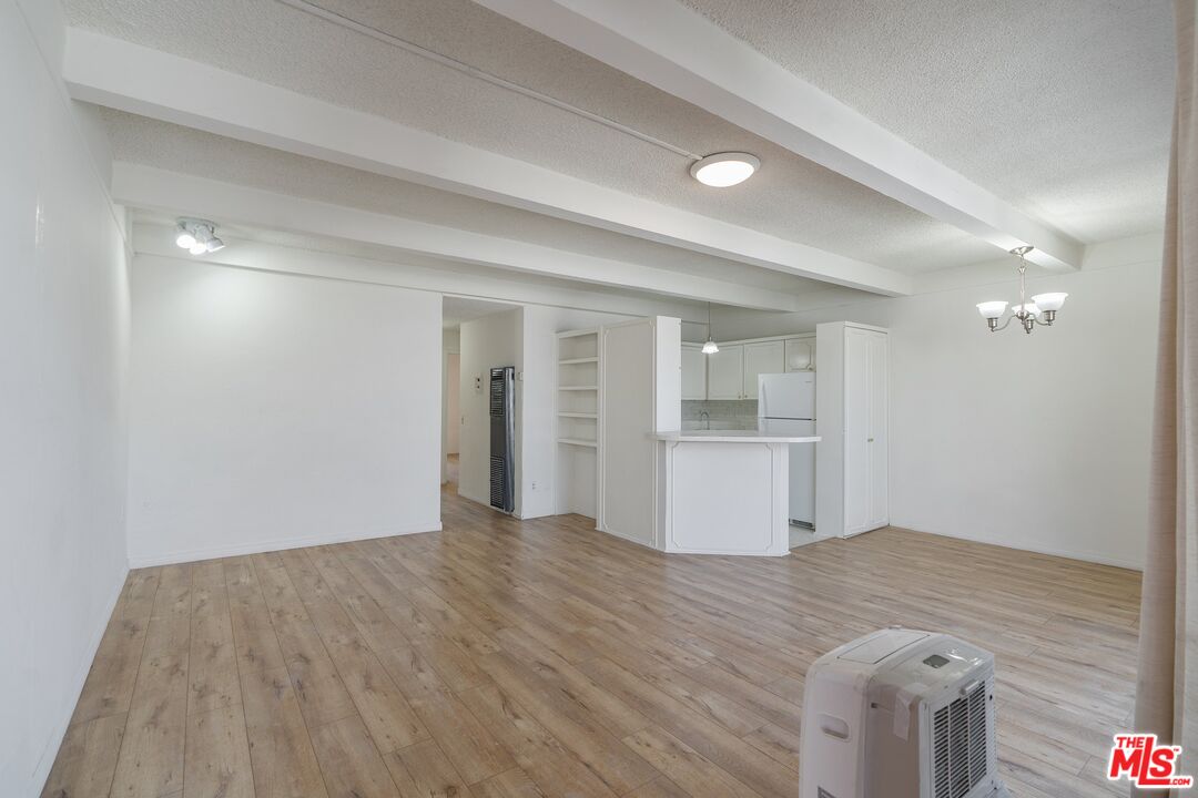 a view of an empty room with wooden floor and a kitchen