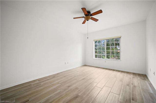 an empty room with wooden floor ceiling fan and windows