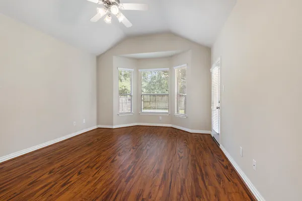 an empty room with wooden floor chandelier fan and windows
