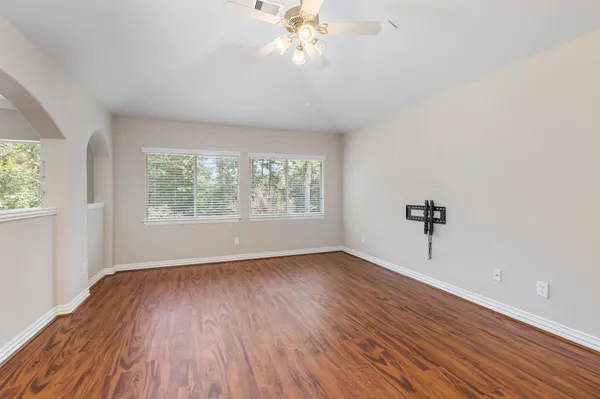 an empty room with wooden floor chandelier fan and windows
