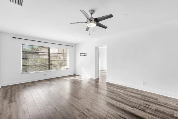 an empty room with wooden floor fan and windows