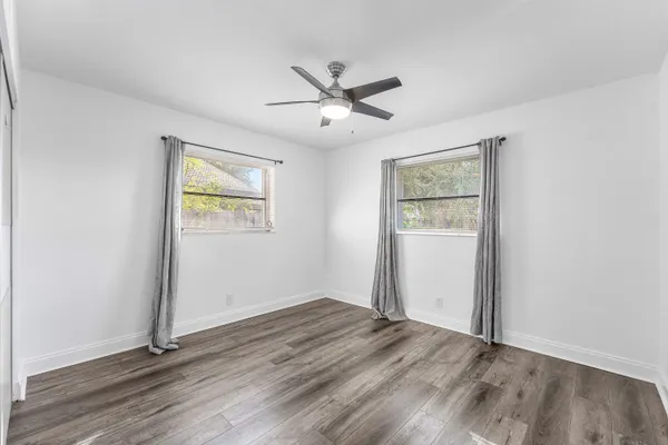 an empty room with wooden floor ceiling fan and windows