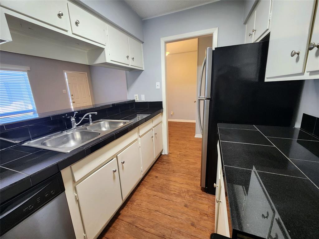 608 West 51st Street, Unit 101 Austin, TX 78751 - Photo 6 of 11 Kitchen with white cabinetry, light wood finished floors, stainless steel appliances, and tile counters