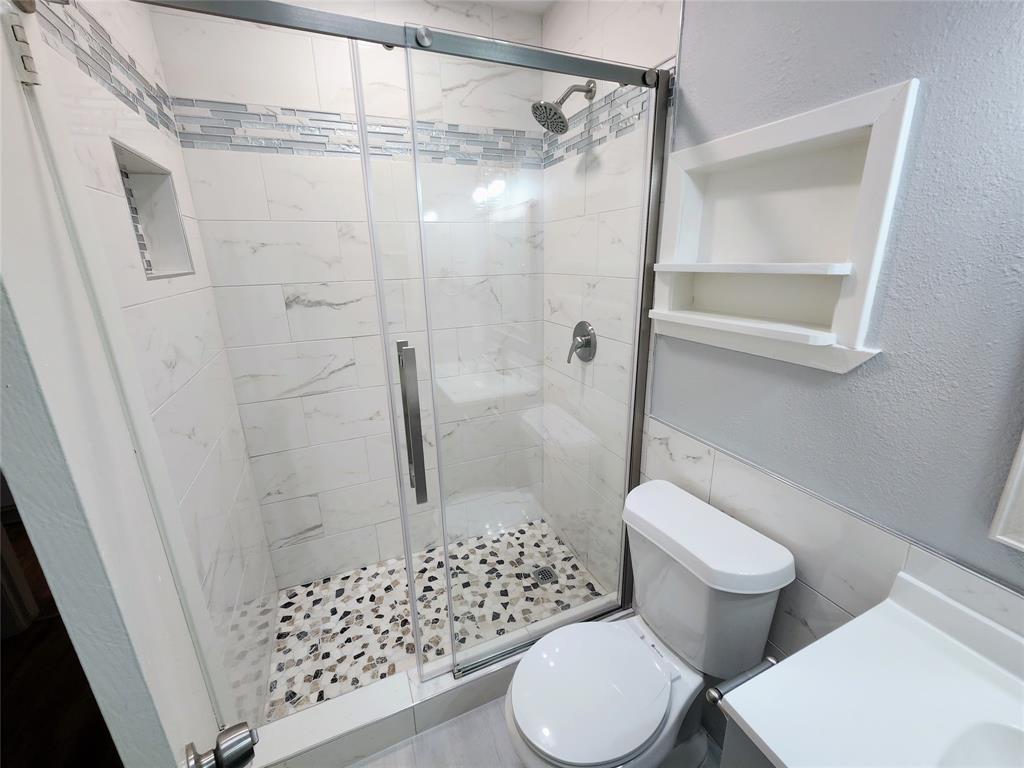 608 West 51st Street, Unit 101 Austin, TX 78751 - Photo 10 of 11 Bathroom with a textured wall, a shower stall, tile walls, vanity, and a wainscoted wall