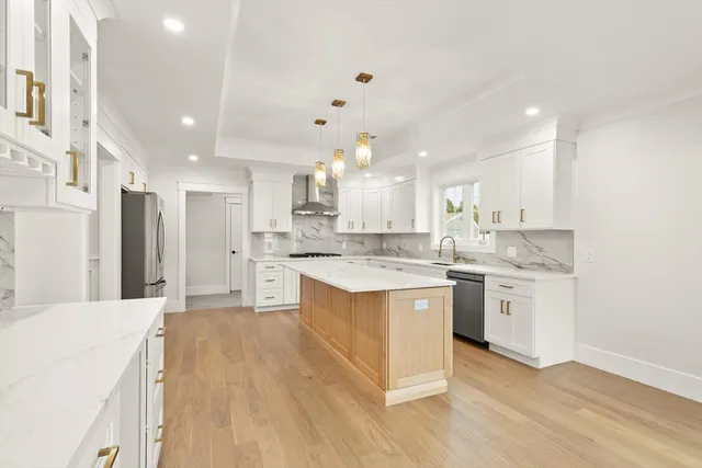 a large kitchen with kitchen island a sink a stove a refrigerator and white cabinets with wooden floor