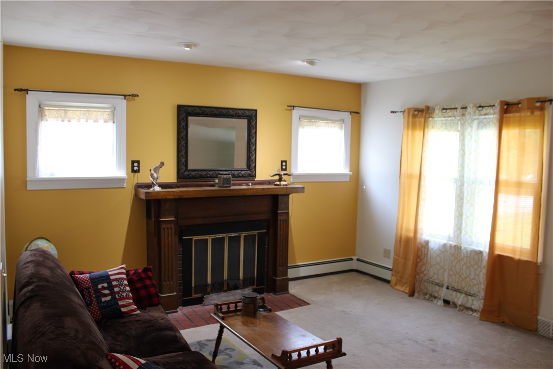 Carpeted living room with a fireplace with flush hearth and baseboard heating
