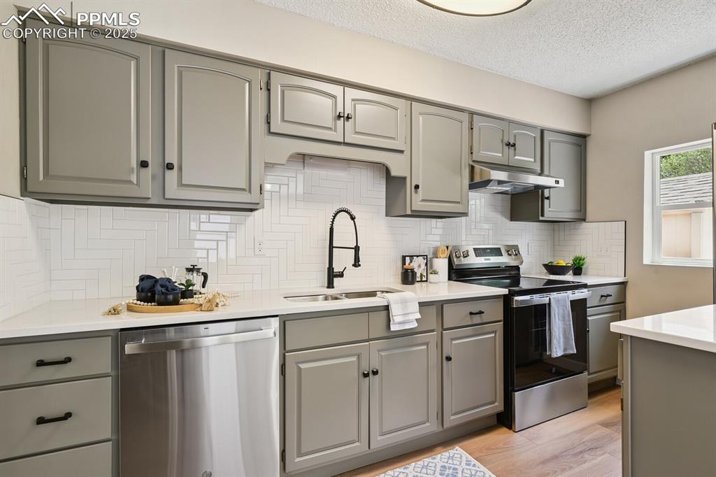 79 Old Broadmoor Road Colorado Springs, CO 80906 - Photo 15 of 27 Kitchen with appliances with stainless steel finishes, gray cabinetry, under cabinet range hood, light wood-type flooring, and a textured ceiling