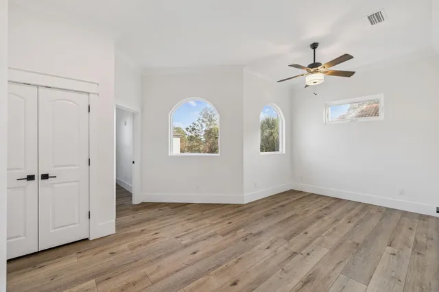 an empty room with wooden floor chandelier fan and windows