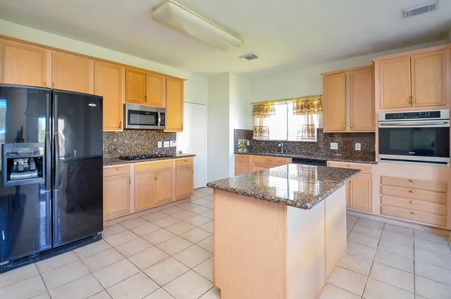 a kitchen with granite countertop a sink a stove top oven a refrigerator and cabinets