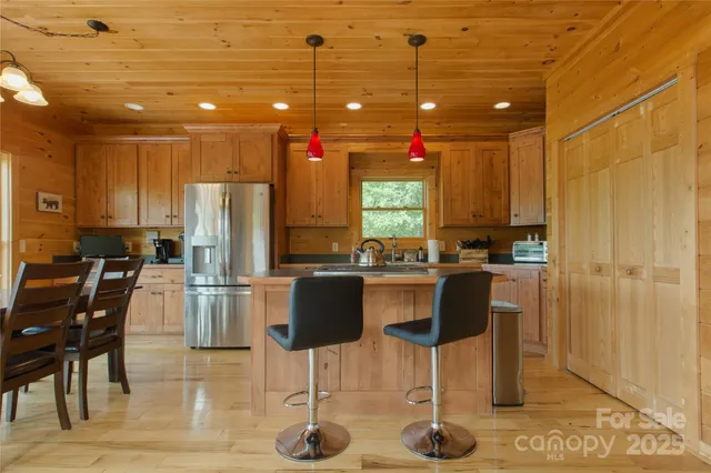 a kitchen with stainless steel appliances kitchen island granite countertop a refrigerator a stove a dining table and chairs with wooden floor