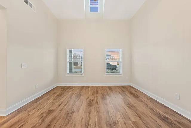 an empty room with wooden floor ceiling fan and windows
