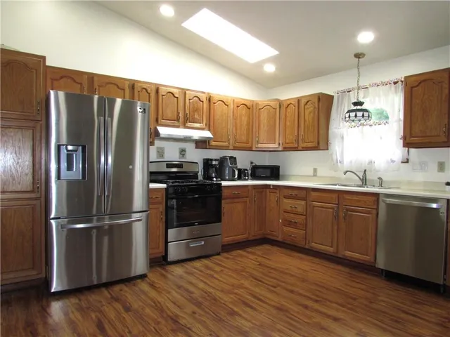 a kitchen with stainless steel appliances granite countertop a refrigerator a sink dishwasher a stove with wooden floors and cabinets