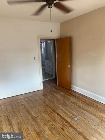 a view of an empty room with wooden floor and a ceiling fan
