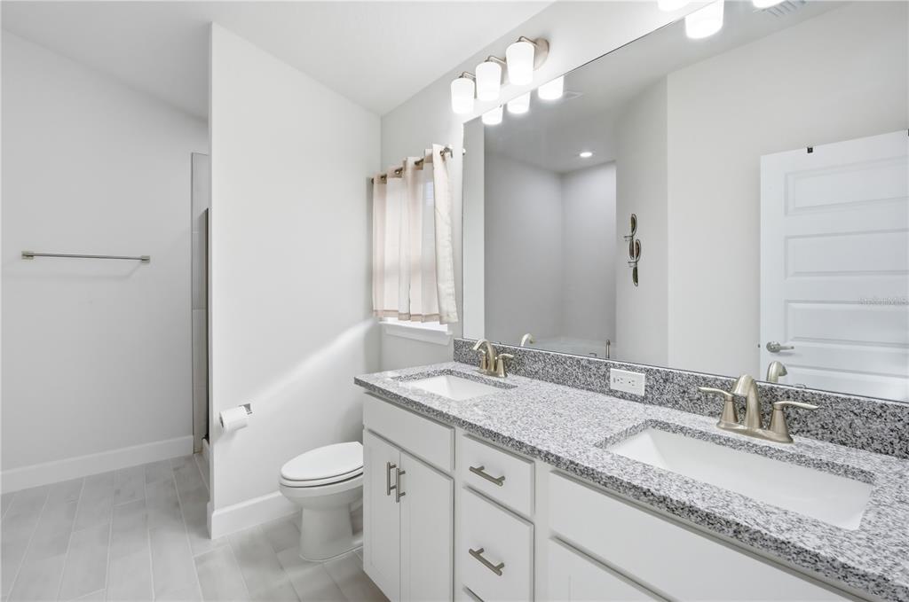 12945 Ogden Glade Road Dade City, FL 33525 - Photo 20 of 26 a bathroom with a granite countertop sink a toilet and a mirror