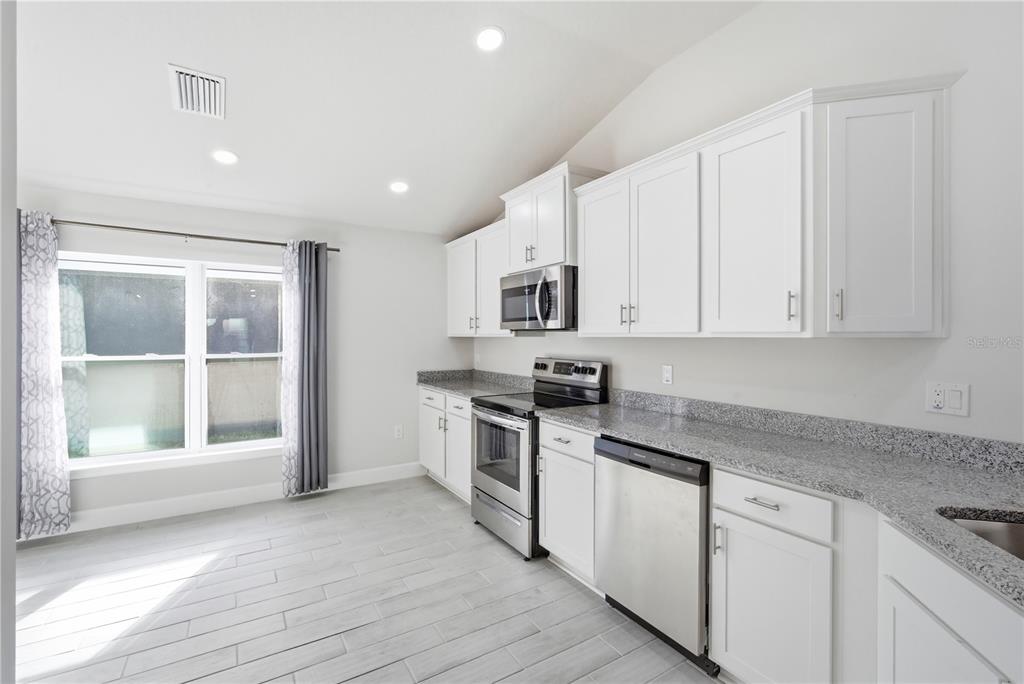 12945 Ogden Glade Road Dade City, FL 33525 - Photo 8 of 26 a kitchen with stainless steel appliances granite countertop a stove a sink and white cabinets