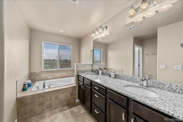 a bathroom with a granite countertop double vanity sink a large mirror and a bathtub