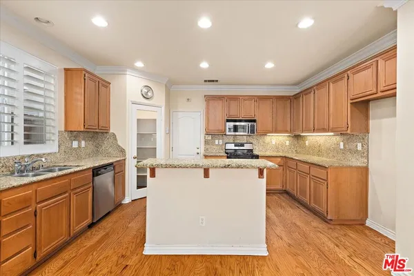 a kitchen with stainless steel appliances granite countertop a stove top oven a sink dishwasher and a refrigerator with wooden floor