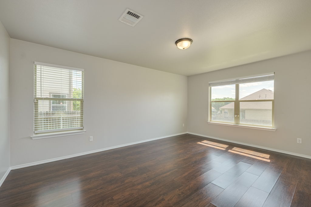 210 Cushman Drive Kyle, TX 78640 - Photo 13 of 21 Spacious room featuring rich wood-finish flooring, light neutral wall paint, and two large windows with blinds
