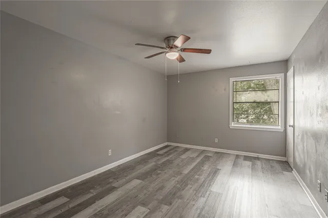 an empty room with wooden floor ceiling fan and windows