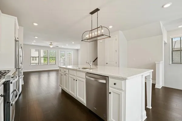 a kitchen with stainless steel appliances kitchen island granite countertop a stove a sink a refrigerator and white cabinets with wooden floor