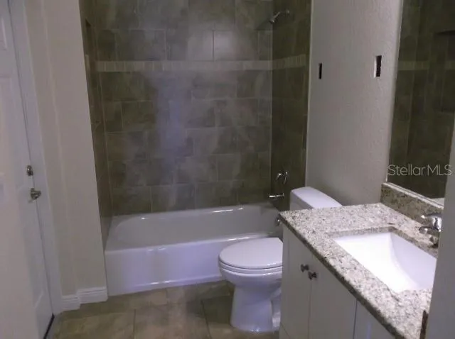a bathroom with a granite countertop bathtub sink vanity mirror and toilet