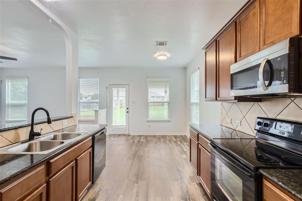 131 Lavaca Loop Hutto, TX 78634 - Photo 7 of 29 An open concept kitchen features warm wood cabinetry and durable flooring, connecting seamlessly to outdoor access.
