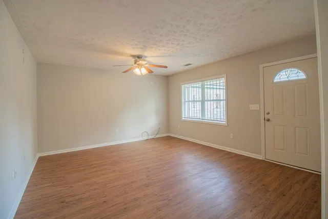 an empty room with wooden floor chandelier fan and windows