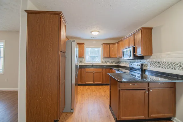 a kitchen with stainless steel appliances granite countertop a refrigerator a sink dishwasher and a stove with wooden floor