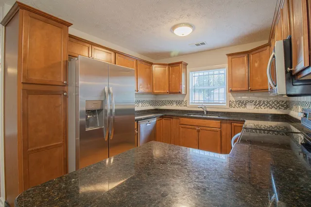 a kitchen with stainless steel appliances granite countertop a refrigerator a sink a stove with wooden cabinets
