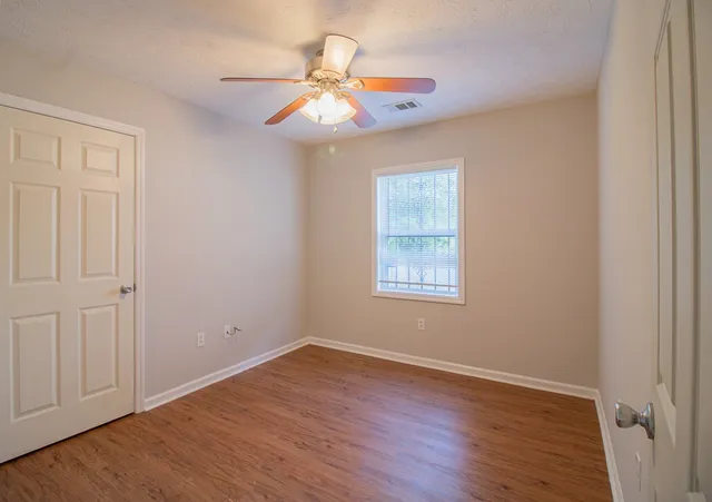 an empty room with wooden floor fan and windows
