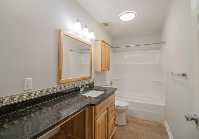 a bathroom with a granite countertop sink a toilet a mirror and shower