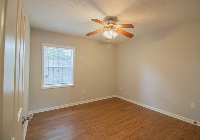 an empty room with wooden floor fan and windows