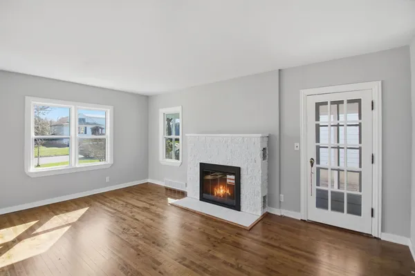 a view of an empty room with wooden floor fireplace and a window