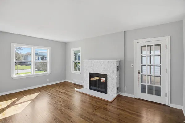 a view of an empty room with wooden floor fireplace and a window