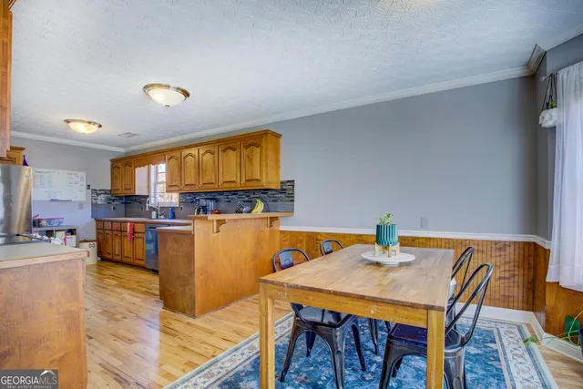 a kitchen with stainless steel appliances granite countertop a refrigerator a sink dishwasher a stove a dining table and chairs with wooden floor