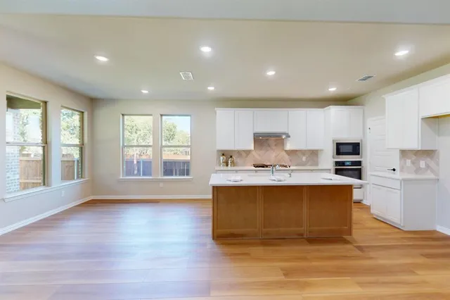 a view of kitchen with stainless steel appliances granite countertop a stove a sink a refrigerator and white cabinets with wooden floor