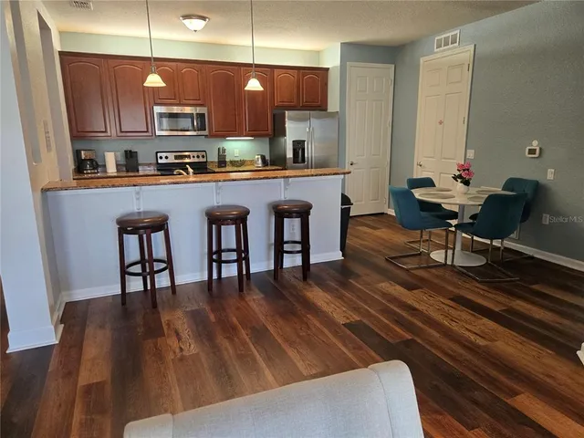 a open kitchen with stainless steel appliances granite countertop a stove top oven a sink a dining table and chairs with wooden floor