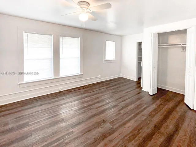 an empty room with wooden floor closet and windows