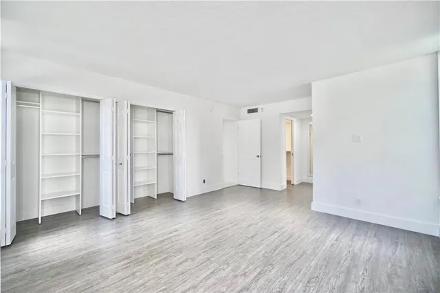 an empty room with wooden floor closet and windows
